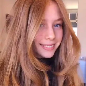 Young woman with long, voluminous strawberry blonde hair featuring face-framing layers and a bouncy blowout style.