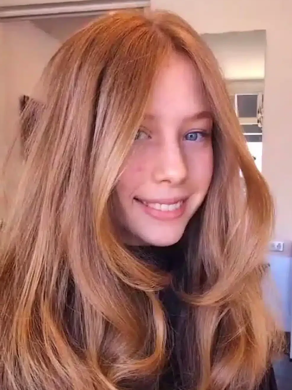 Young woman with long, voluminous strawberry blonde hair featuring face-framing layers and a bouncy blowout style.